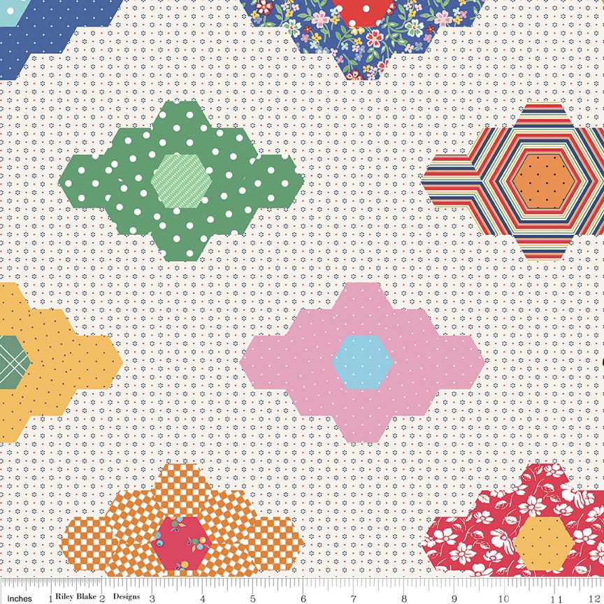 Colorful geometric patchwork pattern on a white background fabric with a ruler at the bottom.
