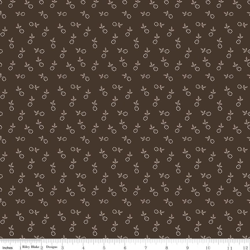 A close-up of a fabric pattern featuring a repeating small floral motif in cream on a dark brown background, with a ruler scale visible along the bottom edge.