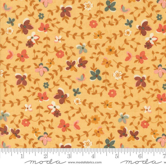 A close-up of a fabric pattern featuring small flowers and leaves in muted orange, pink, brown, green, and white on a warm yellow background, with a measuring ruler along the bottom edge and Modas Fabrics branding.