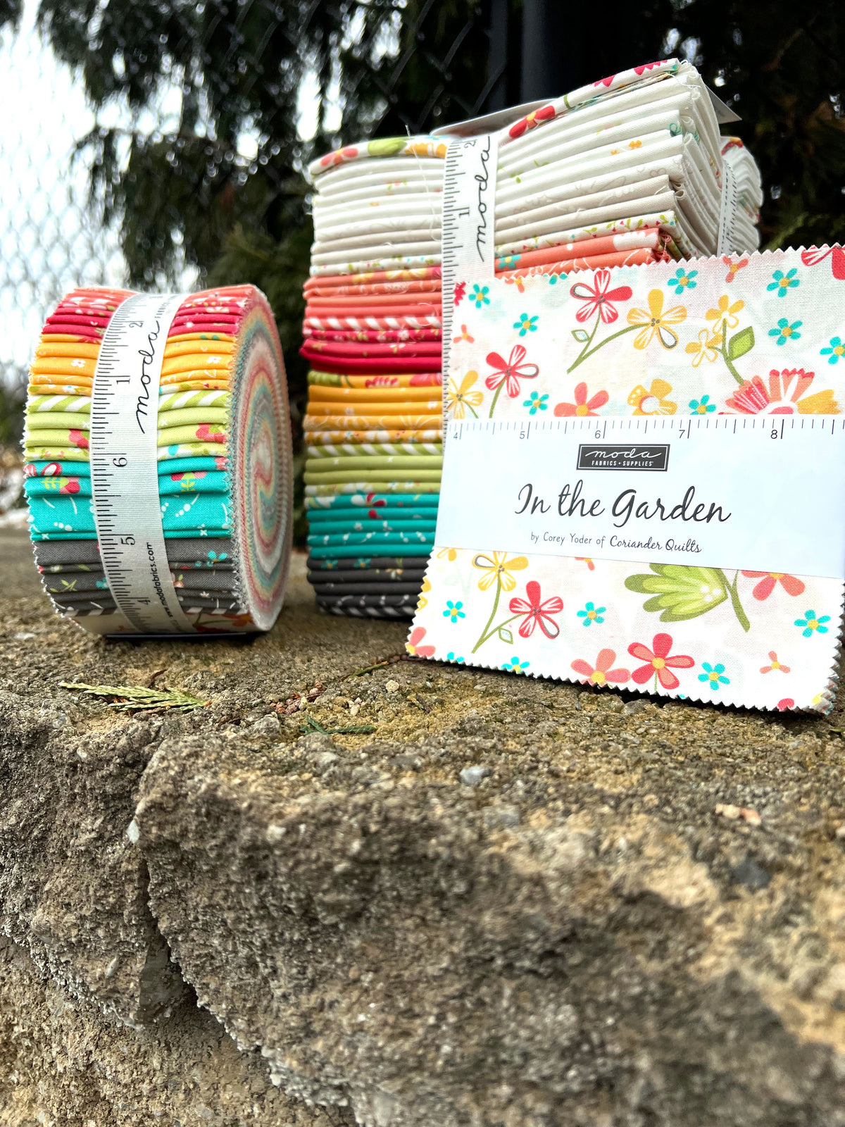 A set of colorful quilted fabric rips and a matching fabric cloth bundle labeled 'In the Garden' by Easy Peasy of Crafter Co, displayed outdoors on a stone surface with a measuring tape and tree background.