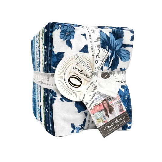 A bundle of fabric quilts wrapped in a white ribbon with a measuring tape design and a bow, featuring a blue floral pattern on a white background. A tag on the ribbon reads 'moda fabric supplies'.