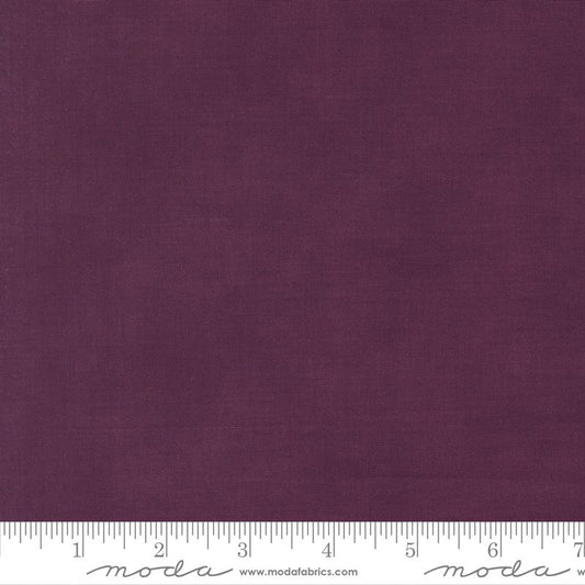 A close-up of a solid deep plum purple fabric texture with a white ruler along the bottom edge showing measurement markings and Modla branding.