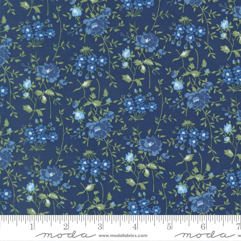 A close-up of a floral fabric pattern featuring blue and light blue flowers with green leaves on a dark navy blue background, with a measuring ruler along the bottom edge showing the scale.