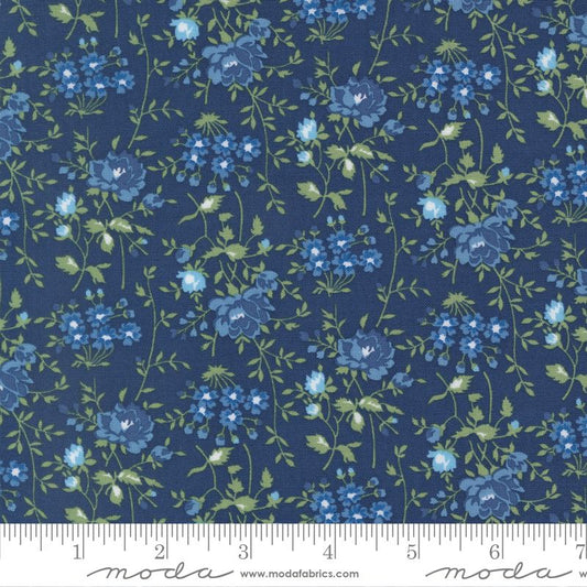 A close-up of a floral fabric pattern featuring blue and light blue flowers with green leaves on a dark navy blue background, with a measuring ruler along the bottom edge showing the scale.