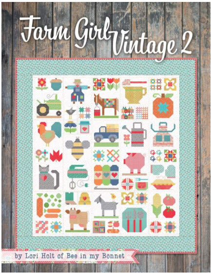 A quilt pattern book titled 'Farm Girl Vintage 2' by Lori Holt of Bee in my Bonnet, featuring a colorful grid of rustic farm-themed patchwork motifs like a tractor, pig, bee, and flowers on a white quilt background, set against a rustic wood plank backdrop.
