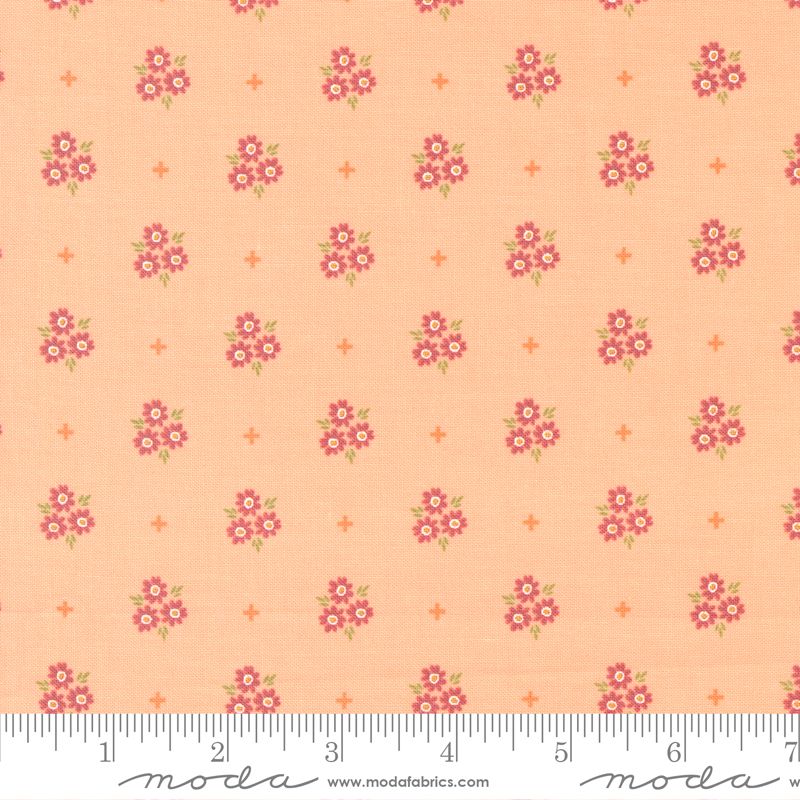 A close-up of a fabric pattern featuring small pink and white floral bouquets with green leaves on a peach background, interspersed with tiny orange stars. A white ruler is visible along the bottom edge to show scale.