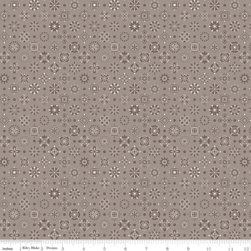 A repeating fabric pattern in pewter, dark gray, and white featuring geometric medallions, stars, and floral motifs, with a ruler scale along the bottom edge.