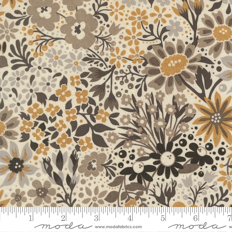 A close-up of a floral fabric pattern with large and small flowers, leaves, and dots in beige, brown, gold, and black, shown with a ruler along the bottom edge. The brand name Moda is visible in script on the ruler.