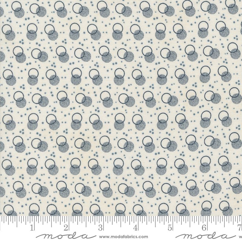 A close-up of a fabric pattern featuring a repeating motif of interlocking rings and dots in dark blue-gray on a warm off-white background, with a ruler along the bottom edge showing measurements.