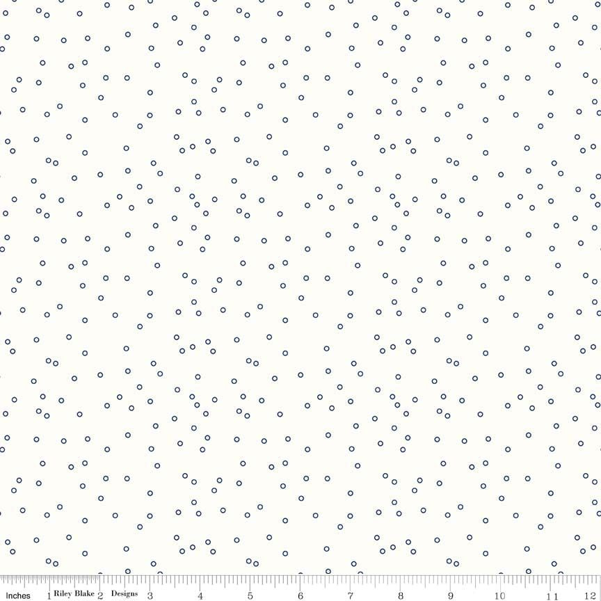 A fabric pattern swatch featuring small, randomly spaced navy blue dots on a warm white background, with a ruler visible along the bottom edge.
