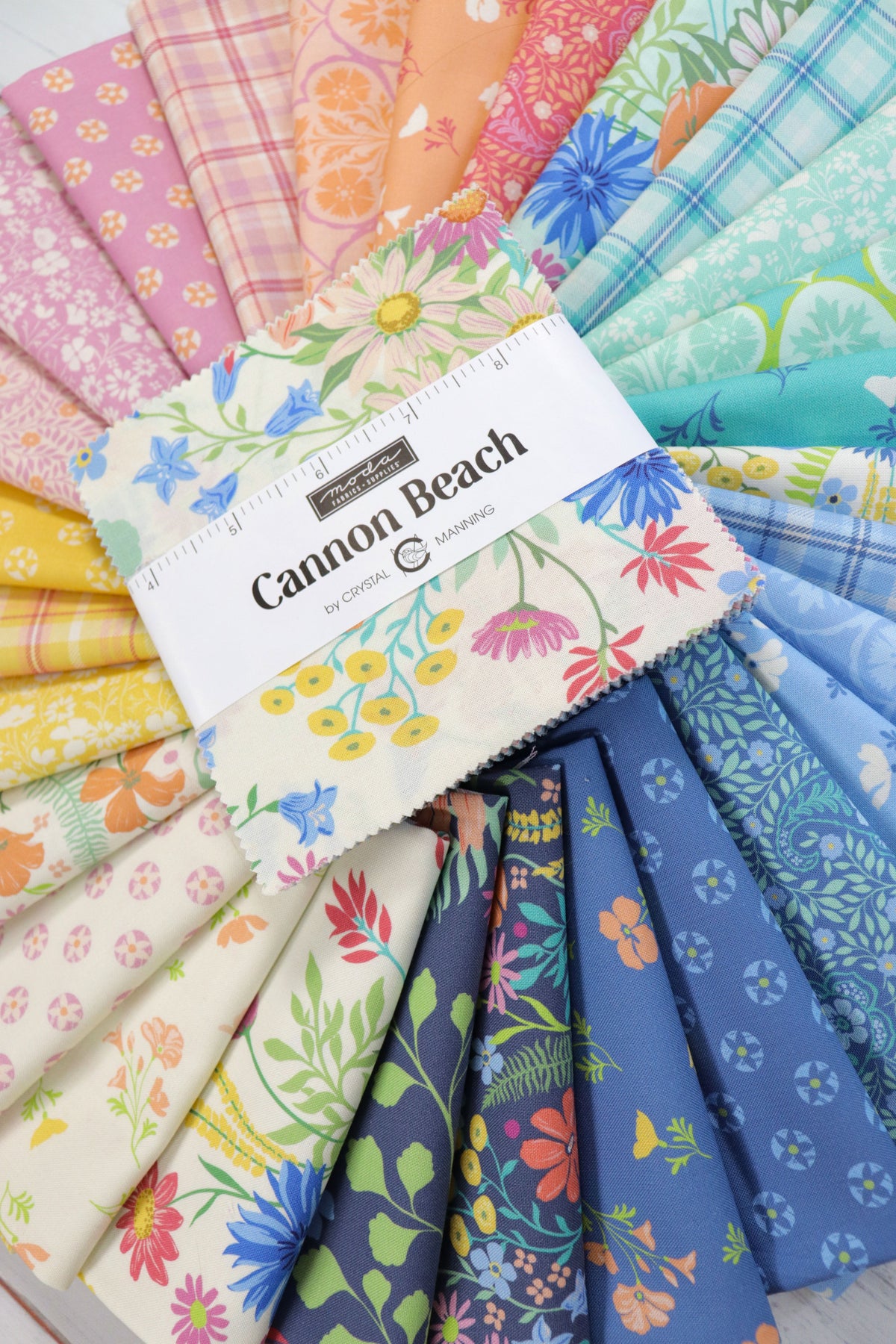 A fanned-out display of colorful fabric samples with floral and patterned prints, centered by a white paper label reading 'Cannon Beach'.