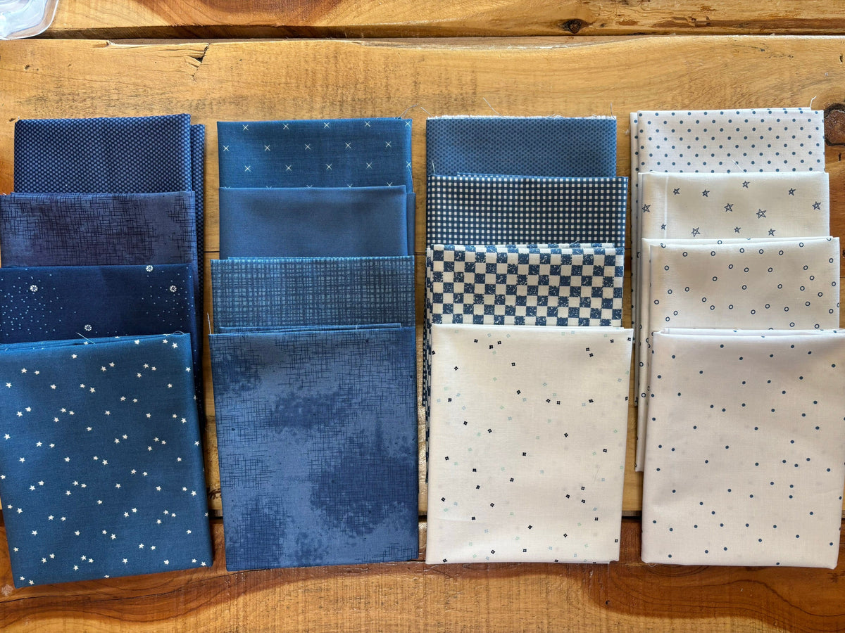 A set of twelve folded fabric squares in various blue and white patterns, arranged in three columns on a wooden surface.