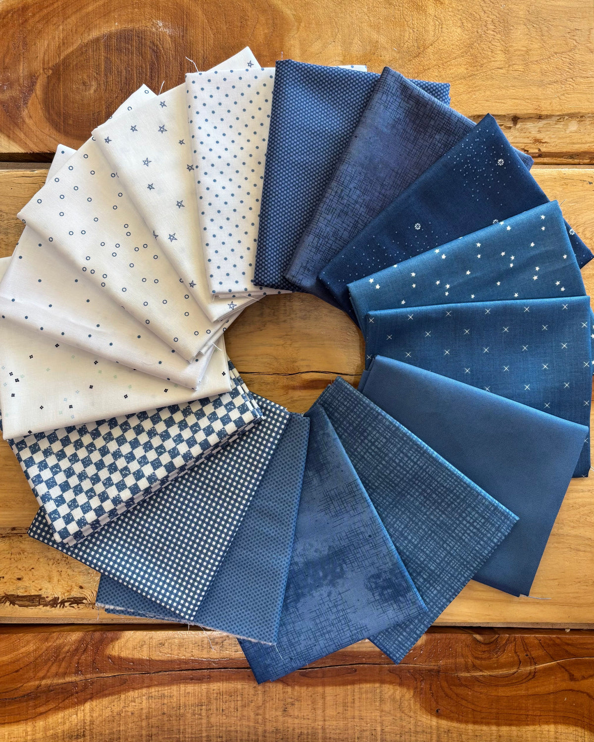 A circular arrangement of blue and white patterned fabric swatches, including polka dots, gingham, and star prints, displayed on a rustic wooden surface.