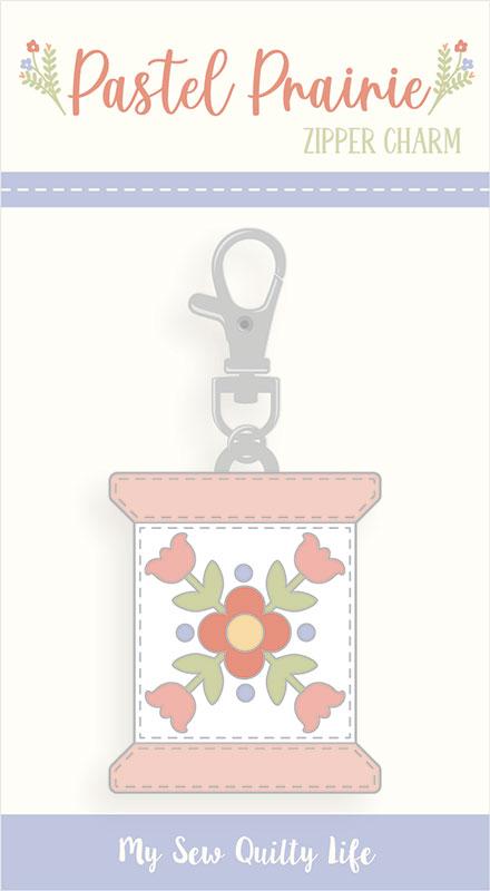 Zipper charm with floral design on a white background.  The charm is in the shape of a thread spool. 