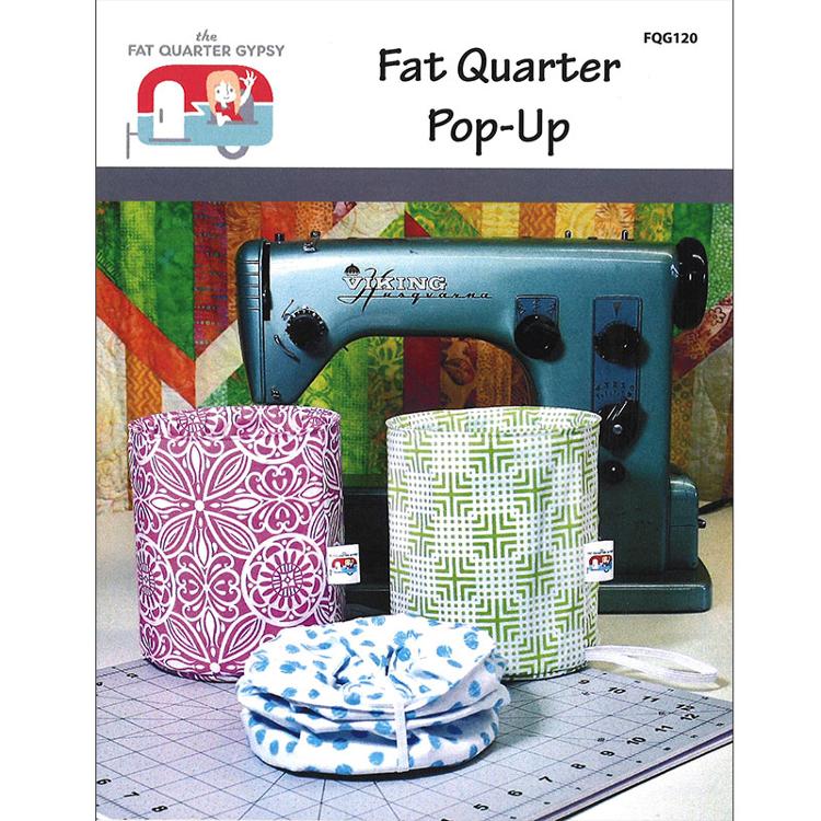 Pattern cover for 'Fat Quarter Pop-Up' by The Fat Quarter Gypsy, showing three fabric-covered cylindrical holders in pink, green, and blue patterns, along with a folded blue-and-white polka dot fabric cover, set in front of a sewing machine on a quilting mat.