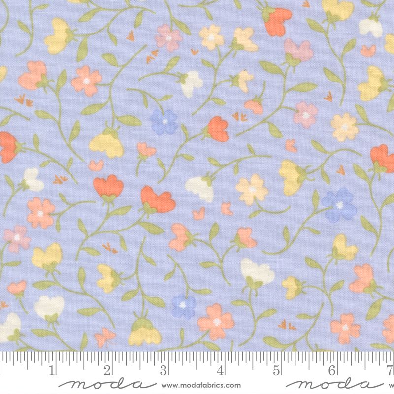 A close-up of a fabric pattern featuring small pastel flowers and green vines on a light blue background, with a ruler along the bottom edge showing measurements. The word 'moda' and 'www.
