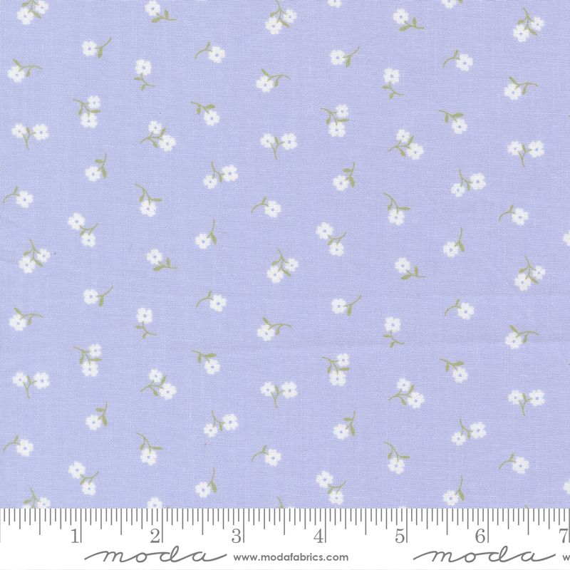 Light blue fabric with a repeating pattern of small white flowers and green stems, shown with a measuring ruler along the bottom edge.