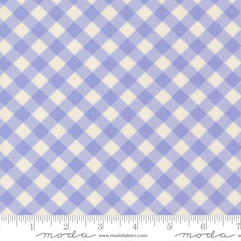 A close-up of a fabric pattern with a pale blue and off-white gingham check design, featuring a ruler along the bottom edge for scale. The brand name 'Moda Fabrics' is visible at the bottom.