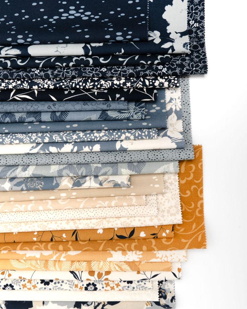 A stack of folded fabric swatches with various floral and geometric patterns in navy, blue, gray, beige, cream, and mustard yellow, arranged neatly on a white background.