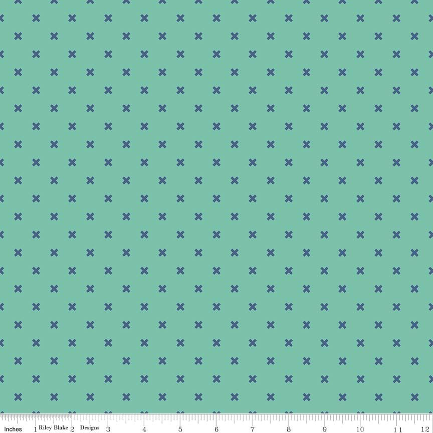 A repeating fabric pattern featuring small royal blue Xs on a teal background, with a white ruler along the bottom edge showing measurements.