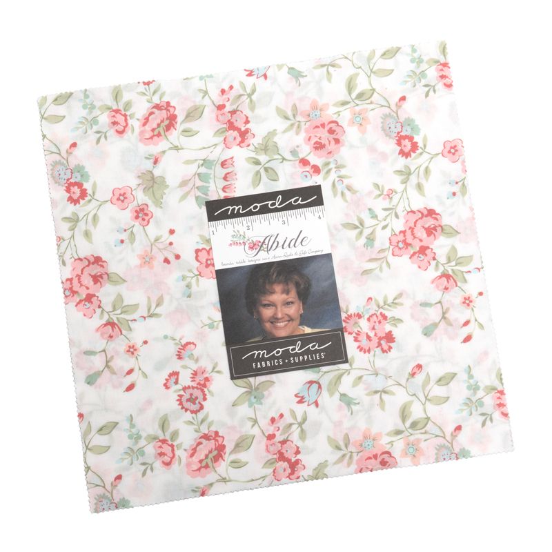 A packaged layer cake from Moda Fabrics, featuring a floral pattern with pink and blue flowers, green leaves, and light blue accents on a white background. The package includes a central label with a photo of the designer, Brenda Riddle