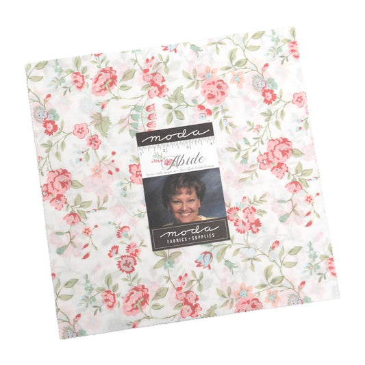 A packaged layer cake from Moda Fabrics, featuring a floral pattern with pink and blue flowers, green leaves, and light blue accents on a white background. The package includes a central label with a photo of the designer, Brenda Riddle