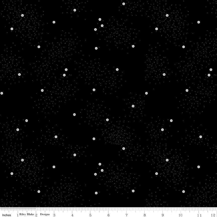 Black fabric with small white daisies and tiny white polka dots and a ruler at the bottom for scale.