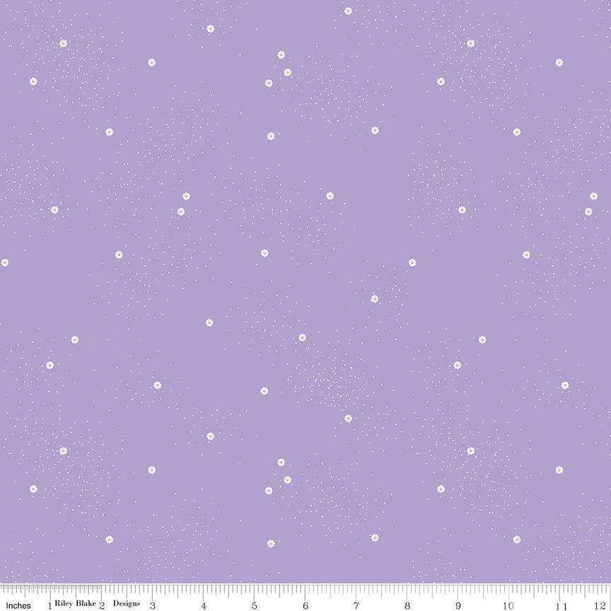 Lavender purple fabric with a white speckled daisy and starry pattern and a ruler at the bottom showing scale.