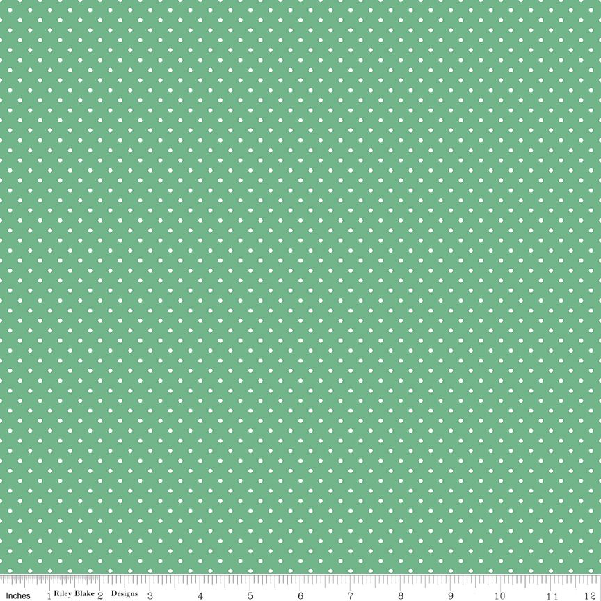 Green fabric with a repeating pattern of small white dots, shown flat with a measuring ruler along the bottom edge.