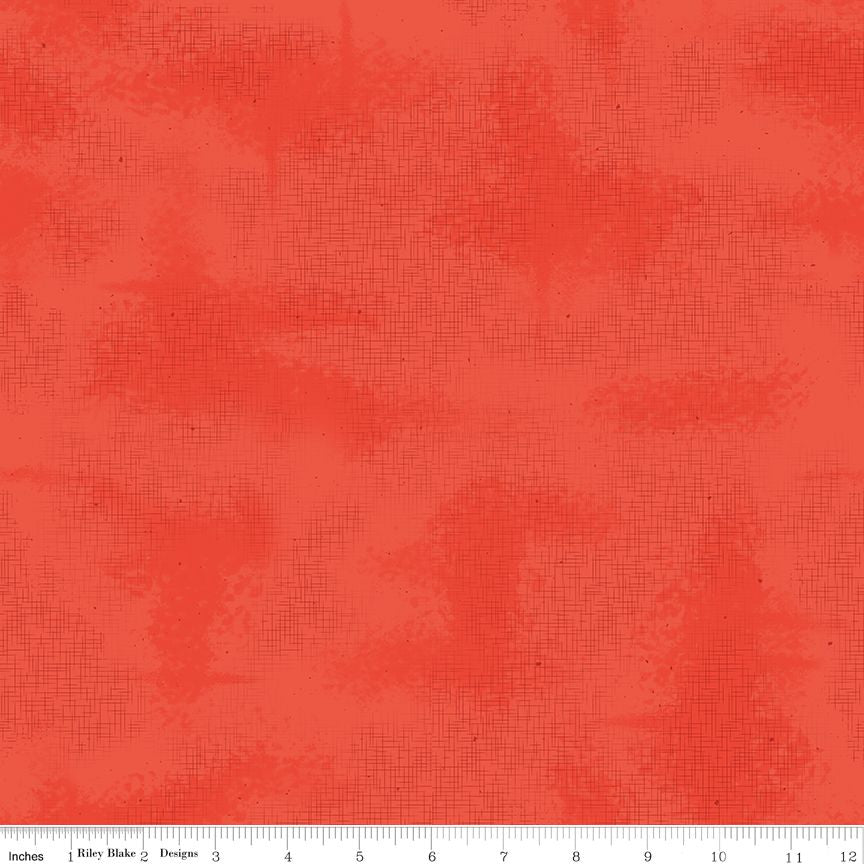 A close-up of a coral red textured fabric with a fine crosshatch pattern, featuring a white ruler at the bottom edge with inch markings.