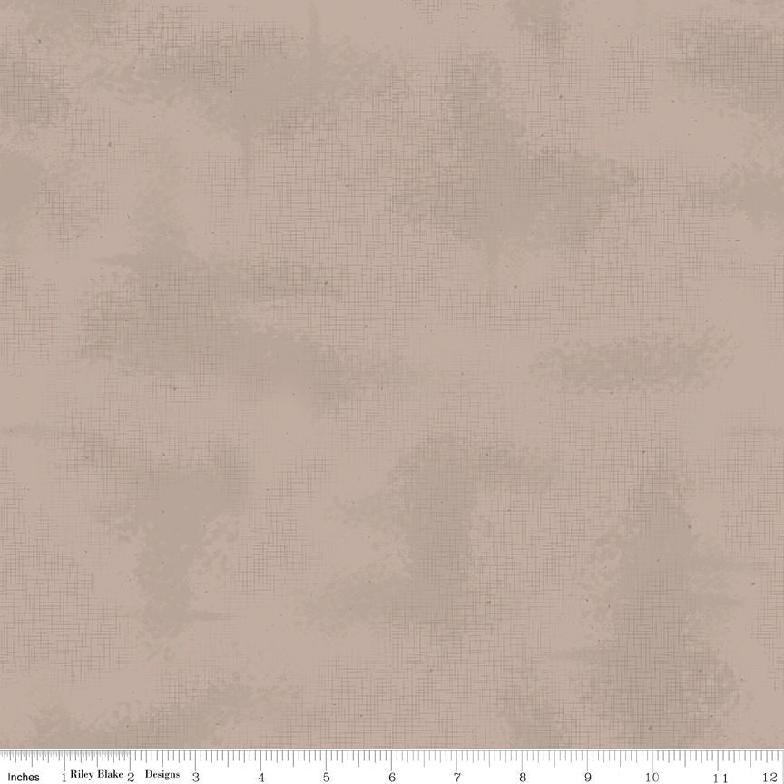 A close-up of a fabric or material swatch in a warm taupe-beige color with a subtle mottled texture. A small ruler scale and printed text appear along the bottom edge.