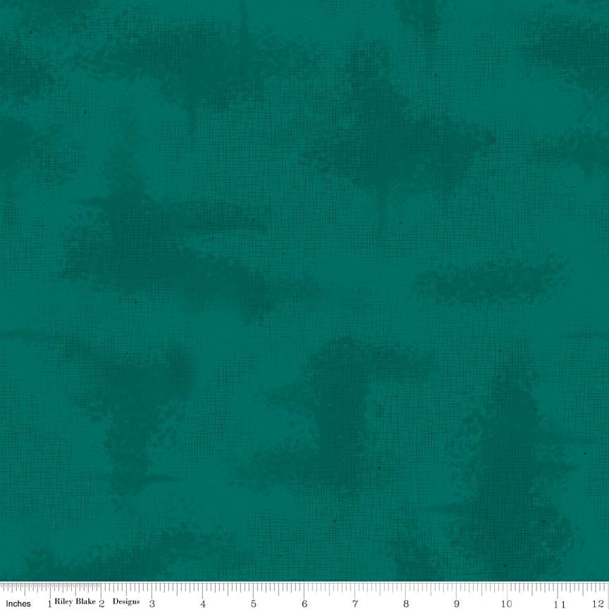 A close-up of a teal fabric with a dark teal abstract distressed pattern, featuring a white ruler scale at the bottom indicating inches and a designer label.