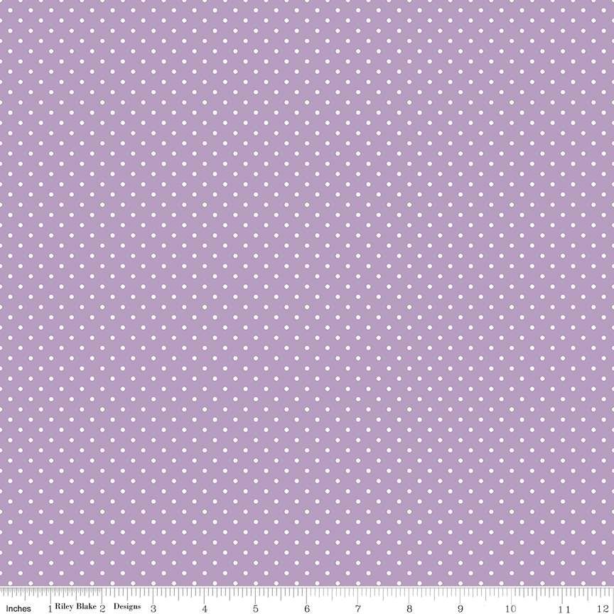 A repeating pattern of small white dots on a light lavender-purple fabric background, with a measuring ruler visible along the bottom edge.
