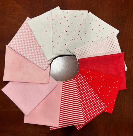A circular arrangement of red and pink patterned fabric squares on a dark wood background, with a silver circular object visible in the center.