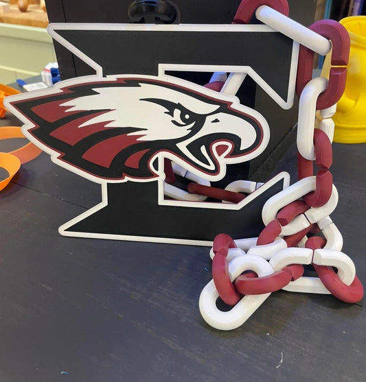A black E featuring an Eagleville eagle head logo in white, burgundy, and black, with a burgundy and white chain draped over the right side, photographed on a dark tabletop.