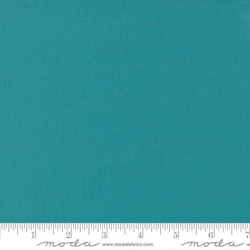 A close-up of a solid teal fabric texture with a white ruler along the bottom edge showing measurement markings and Modra branding.