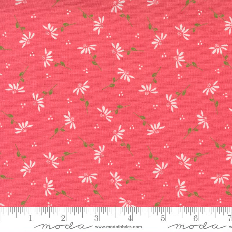 A close-up of a fabric pattern featuring small white daisy-like flowers and green stems on a coral pink background, with a white ruler along the bottom edge showing measurement markings and the Moda watermark.