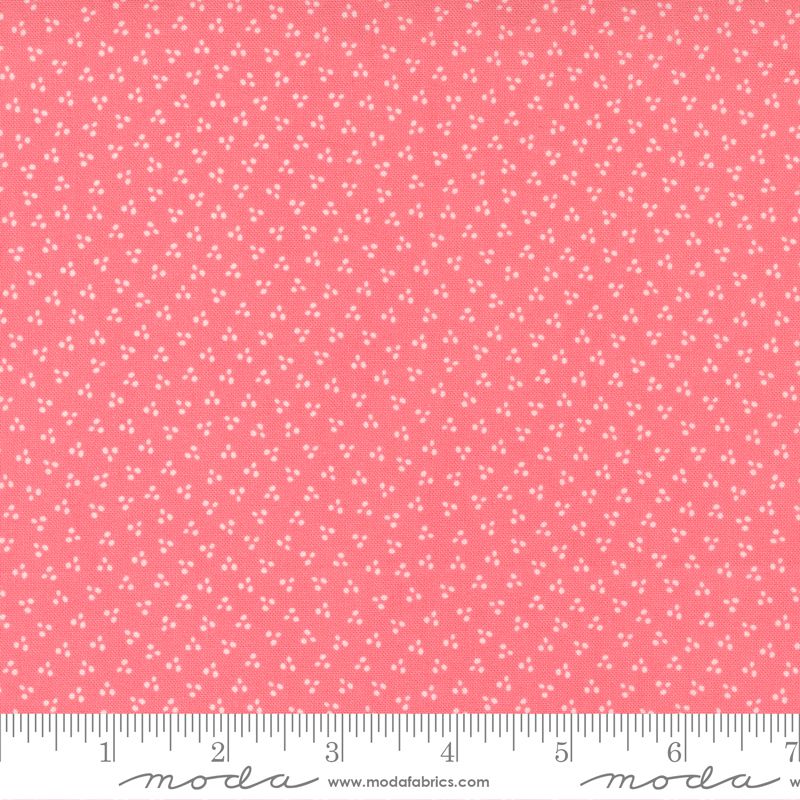 A close-up of a pink fabric with a small white dot pattern, shown with a measuring ruler along the bottom edge to indicate scale. The brand name 'Moda Fabrics' is visible on the ruler.