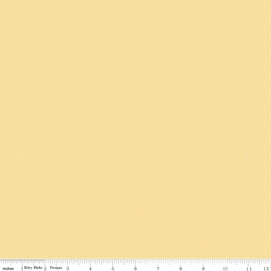 A close-up fabric or material swatch showing a warm yellow background with a repeating small beige polka dot pattern. A ruler along the bottom edge includes branding text for Riley Blake Designs.