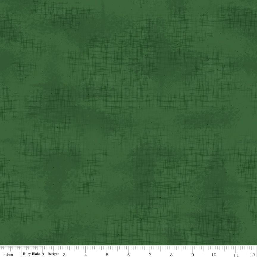 A close-up of a dark green fabric with a subtle textured, distressed pattern. A white ruler at the bottom edge shows the scale of the fabric, indicating the brand Riley Blake Designs.