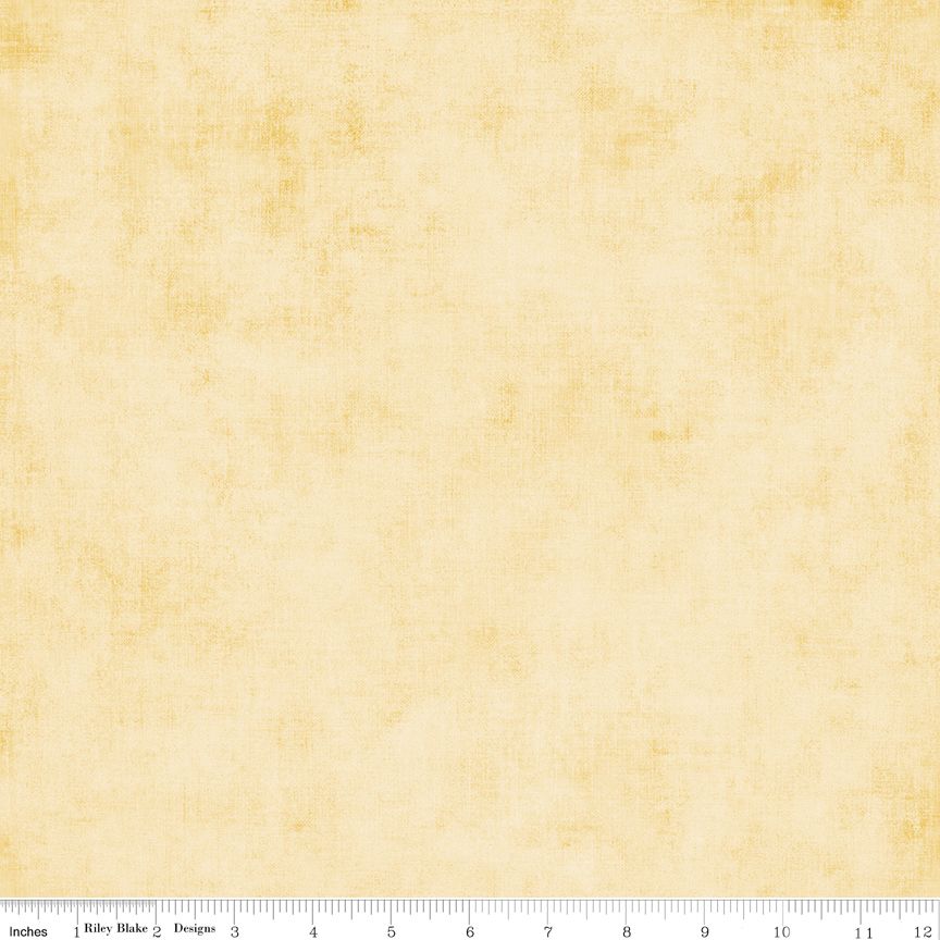 A square fabric or paper swatch in a warm cream-beige tone with subtle yellow mottling and a faint textured pattern, shown with a ruler along the bottom edge for scale.