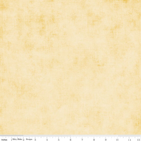 A square fabric or paper swatch in a warm cream-beige tone with subtle yellow mottling and a faint textured pattern, shown with a ruler along the bottom edge for scale.