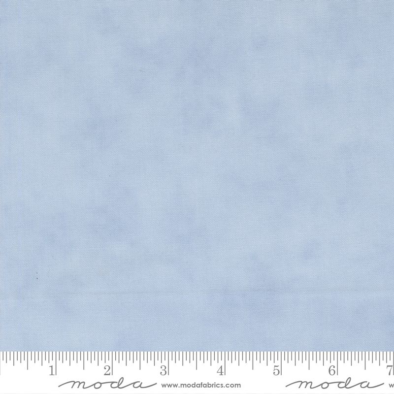 Light blue fabric with a subtle mottled texture, shown with a measuring ruler at the bottom to indicate scale. The brand name 'Moda Fabrics' is visible on the ruler.