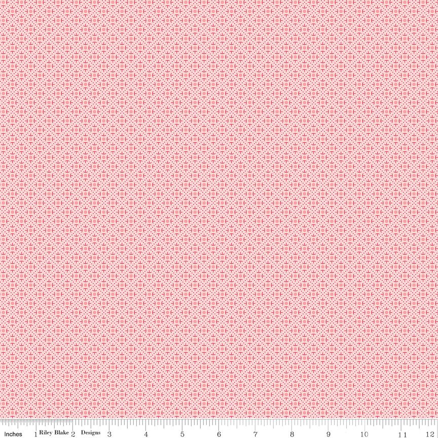 A close-up of a repeating fabric pattern in soft pink and white, with a ruler along the bottom edge showing the scale of the design. The brand name 'Riley Blake Designs' is visible on the ruler.