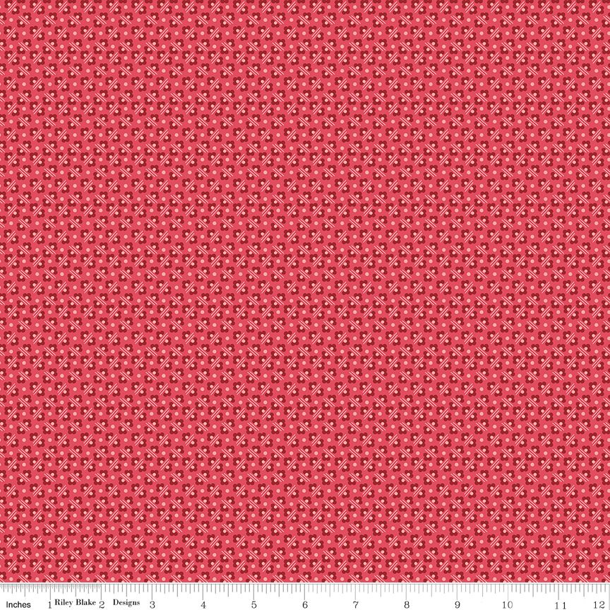 Red fabric with a repeating small black and white geometric pattern, shown flat with a ruler along the bottom edge for scale.