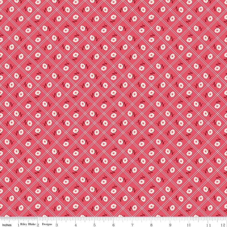 A close-up of a fabric pattern featuring a repeating design of small white flowers on a coral pink background, overlaid with a white diamond grid. A white ruler is visible along the bottom edge.