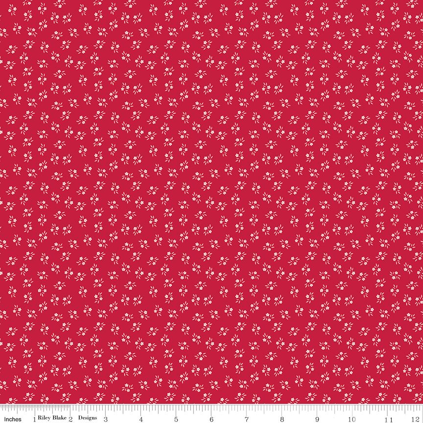 Red fabric with a repeating small white floral pattern, shown flat with a ruler along the bottom edge for scale.