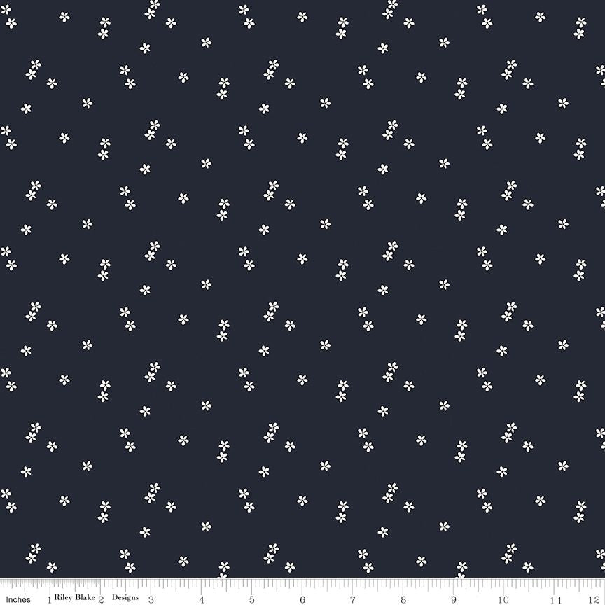 A fabric pattern swatch featuring a dark navy blue background with a scattered print of small white five-petal flowers. A white ruler scale is visible along the bottom edge.