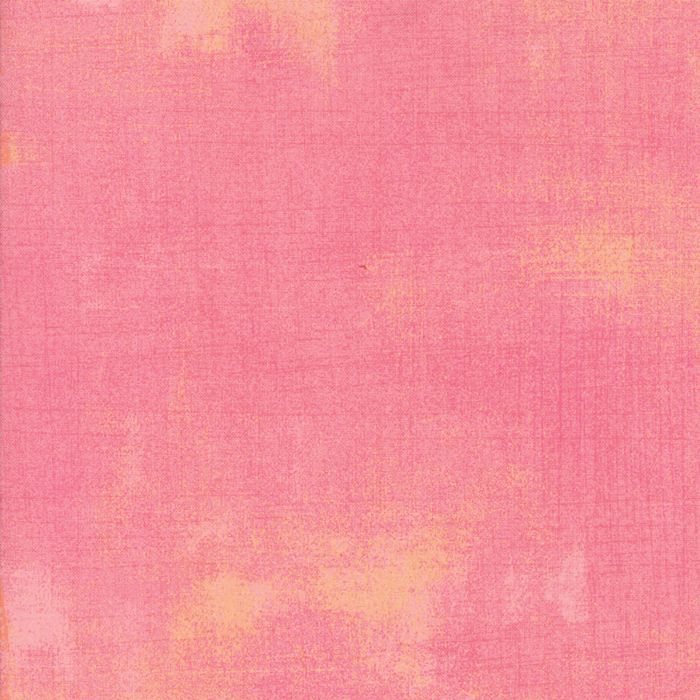 A close-up of a pink textured material with subtle warm yellow-orange mottled areas, filling the frame.