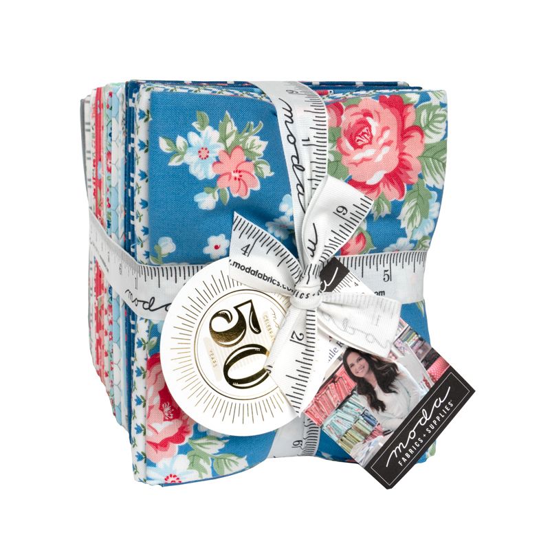 A fat quarter bundle of A Cat Named Stitch fabric line featuring a floral pattern in blue, pink, and white, wrapped with a white measuring ribbon and a round white tag.